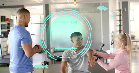 Seated client receiving forearm check in gym studio, trainers in athletic shirts using tablet. Rehab, patient, coaches, monitoring, biometrics, overlay, daylightの写真素材