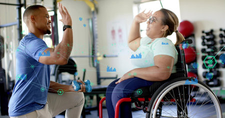 High-fiving woman in red wheelchair in top, kneeling-trainer holding dumbbell, gym, HUD, copy space. Adaptive, rehabilitation, inclusive, strength, training, equipment, daylightの写真素材