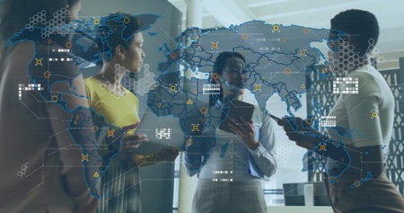 Collaborating women in business attire holding devices gesturing toward holographic map in office....