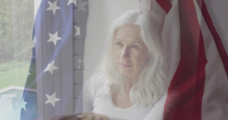 Gazing senior woman sitting by white shuttered window in living room, viewing pool. Residential,...