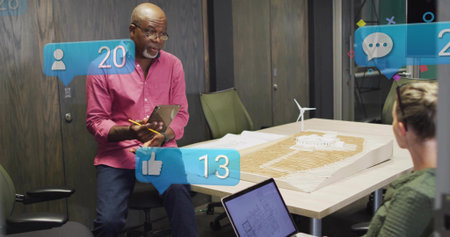 Presenting architect wearing pink shirt and jeans at conference table, with scale model, tablet....