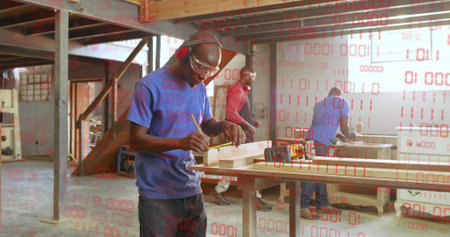 Marking wooden plank male carpenter wearing safety goggles, earmuffs at workshop, with pencil....