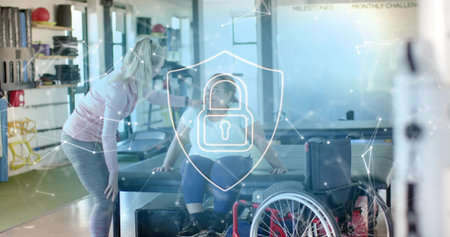 Leaning clinician in pink top guiding patient on gym table, red wheelchair, digital shield overlay. Rehab, therapy, mobility, clinic, equipment, daylight, movementの写真素材