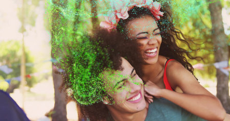 Laughing couple piggybacking in park wearing tshirt amid green powder, flower crown and flags. Festivals, celebration, outdoor, vibrant, youth, joy, leisureの写真素材