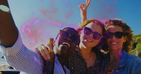 Smiling friends with sunglasses leaning by sea, capturing selfie with beer bottle and color powder. Casual, outdoor, vibrant, celebration, leisure, summer, socialの写真素材