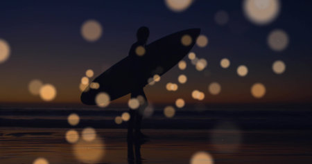Walking wetsuit-clad surfer holding surfboard on wet sand at dusk, with bokeh orbs reflecting sky. Beach, silhouette, sunset, reflection, tranquility, shoreline, wildernessの写真素材