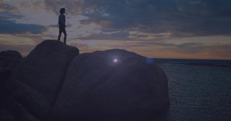 Exploring Asian woman wearing jacket boots on rocky shoreline by calm water at sunset, copy space. Adventure, exploration, nature, landscape, tranquility, silhouette, horizonの写真素材