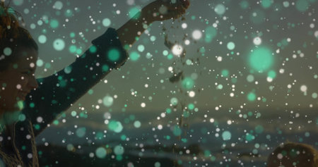 Mother pouring pebbles over infant on shoreline at dusk, with knitted beanie, sweater, copy space. Family, bonding, outdoor, serenity, tenderness, leisure, naturalの写真素材
