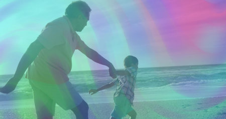 Running grandfather and grandson reaching out holding hands on sandy shoreline, with ocean waves. Family, outdoor, leisure, carefree, connection, adventure, relaxingの写真素材