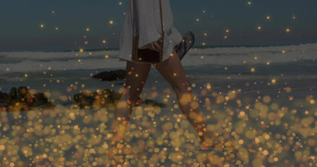 Walking woman wearing white dress leaving footprints on beach, with woven bag, flip-flops and rocks. Coastal, leisure, summer, serenity, nature, minimalism, travelの写真素材