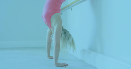 Balancing female dancer wearing pink leotard holding handstand on studio floor with ballet barre. Dance, flexibility, athleticism, movement, elegance, fitness, trainingの写真素材