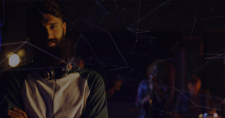 Standing bearded musician crossing arms in studio with headphones, instruments, network overlay....
