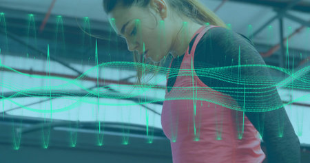 Monitoring woman in pink tank top tracking performance data in gym, in-ear earbuds and waveform....