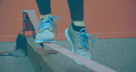 Balancing woman's legs and feet wobbling on slackline at fitness studio, with blue-laced sneakers....