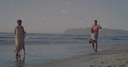 Family walking on beach at sunset with mother wearing dress holding son, father swinging daughter. Beach, sunset, lifestyle, leisure, tranquility, family, natureの写真素材