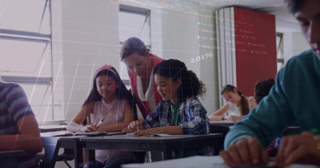 Guiding teacher leaning over two students writing at school desk, with notebooks data projection. Education, classroom, learning, instructional, scholastic, academic, youthの写真素材