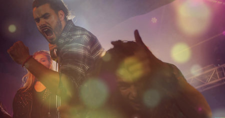 Singing lead vocalist wearing plaid flannel shirt energizing stage, with microphone and spotlights. Live performance, band, music, concert, stage, lighting, atmosphereの写真素材