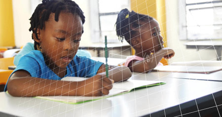 Leaning girl wearing blue shirt writing in notebook with pencil in classroom, copy space. Children, education, learning, classroom, study, brightness, creativityの写真素材