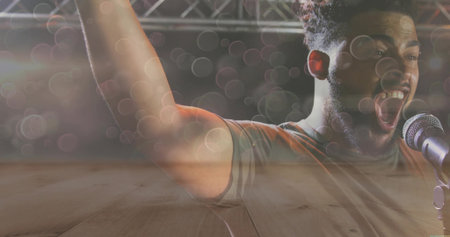 Singing adult male in t-shirt on concert stage with microphone stand and lighting truss, copy space. Performance, music, entertainment, stage, vocalist, celebration, charismaの写真素材