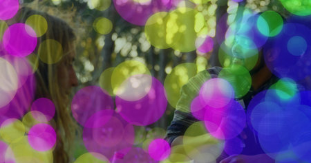 Friends standing in casual tops facing each other in wooded park, with headphones and pink bottle....
