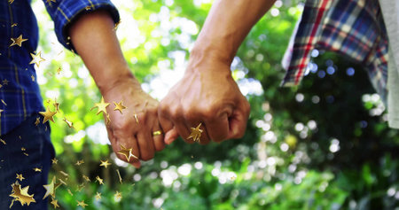 Linking senior couple in plaid shirts hooking pinkies in garden with trees, with gold wedding bands. Commitment, affection, longevity, nature, serenity, harmony, warmthの写真素材