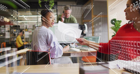 Collaborating woman in striped top holding page turning to colleague at office desk, data overlays....