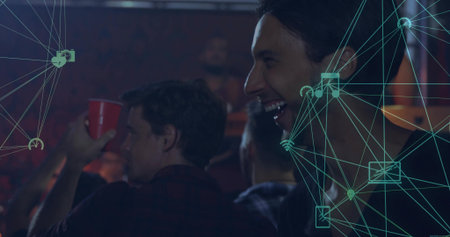 Laughing Black man raising red cup at dim bar counter, with teal network icons, copy space. Socializing, nightlife, celebration, connectivity, urban, vibrant, entertainmentの写真素材