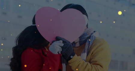 Holding pink heart cutout covering faces on city street, with winter scarves and knitted gloves. Romance, affection, celebration, companionship, warmth, winterfashion, urbansettingの写真素材