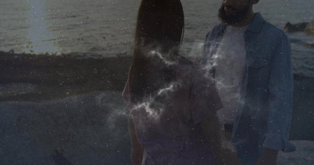 Standing mid adult female facing adult male on rocky shoreline at dusk, reflecting water light. Romantic, beachfront, tranquility, silhouette, nature, connection, intimateの写真素材