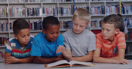 Leaning four school age boys reading open hardcover book in library reading area, with bookshelves. Collaboration, education, literacy, diversity, youthful, concentration, learningの写真素材