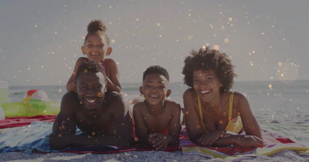 Lying family in swimwear smiling on striped towels at shoreline, with swim ring and beach ball. Family, leisure, lifestyle, vibrant, playful, seaside, relaxationの写真素材