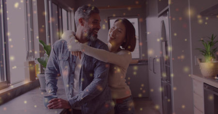 Smiling senior man holding ceramic mug at kitchen counter, with Asian woman hugging shoulders. Cozy, affection, domestic, warmth, companionship, lifestyle, natural lightの写真素材