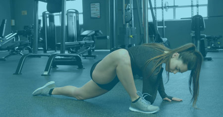 Athlete stretching in gym wearing black workout clothes, with weight benches cable pulley station. Fitness, strength, training, exercise, wellness, health, sportの写真素材