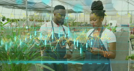 Reviewing tablet two nursery workers examining data overlay amid potted plants, wearing dark aprons....