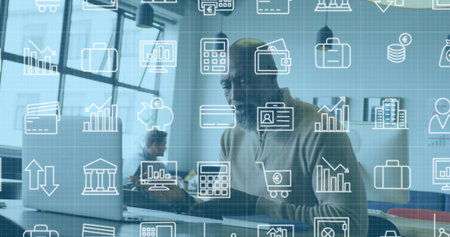 Working Black man wearing light zip sweater typing on laptop in open office, finance icons overlay....