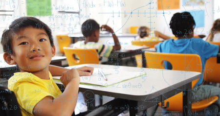 Sitting boy wearing yellow T-shirt writing in workbook at elementary classroom, with math overlay. Bright, students, desks, notebooks, windows, equations, educationの写真素材