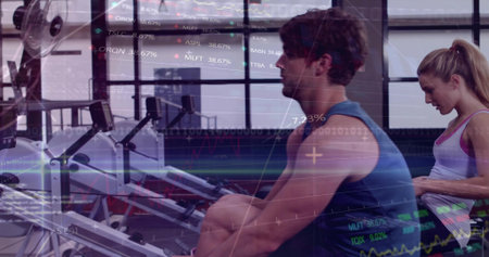 Rowing muscular man wearing blue sleeveless top pulling handle on rower at gym, with charts overlay. Ergometer, fitness, cardio, training, partners, daylight, windowsの写真素材