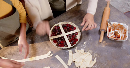 Assembling pair placing pastry lattice over cherry tart on home kitchen counter, wearing yellow top.の写真素材