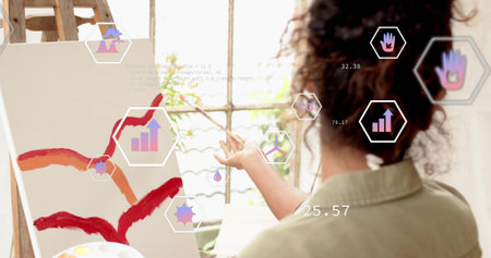 Painting painter wearing tan shirt making red marks at art studio easel, with palette. Artist, woman, window, ladder, natural, light, greeneryの写真素材