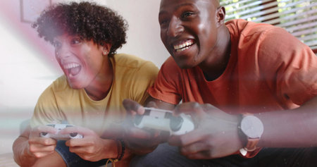 Playing two men leaning on couch at home, holding white gamepads, wearing mustard and orange shirts....