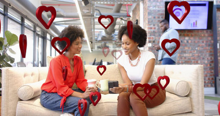 Chatting pair wearing red blouse and white top holding coffee, device on office sofa, red hearts....