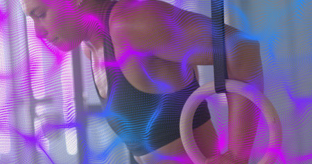 Gripping rings, athlete holding at gym, wearing black sports bra, wrist tape, purple blue overlay. Calisthenics, strength, fitness, studio, dynamic, focus, trainingの写真素材