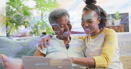 Smiling daughter in yellow shirt pointing at laptop, mother leaning on sofa at home, AR overlay. Family, collaboration, learning, technology, augmented, reality, interactionの写真素材