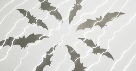 Displaying black paper bat cutouts radiating in studio on white surface with diagonal light streaks. Silhouette, radial, arrangement, motif, symmetry, shadows, decorの写真素材
