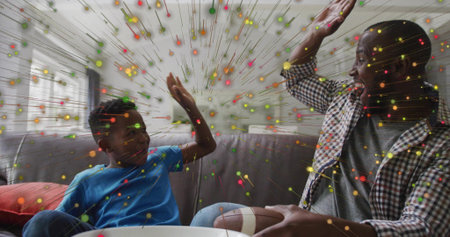 High-fiving dad and son on gray sofa at home, checked-shirt-blue-tee, football-and-bowl, confetti....