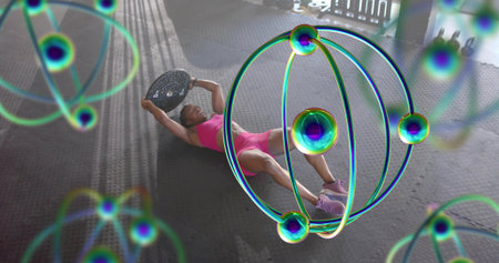 Lying midadult woman in pink holding plate on rubber mats, kettlebells, purple shoes. Fitness, gym,...