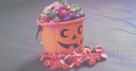 Displaying orange jack-o-lantern bucket holding foil-wrapped sweets on gray table, spilling gummies. Pumpkin, candies, lantern, halloween, studio, stilllife, bokehの写真素材
