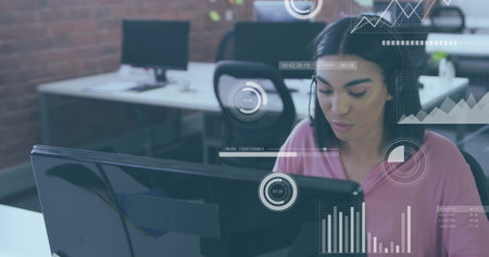 Monitoring woman in pink top with headset studying data on monitor at open office, HUD overlays....