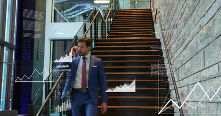 Walking businessman wearing navy suit holding jacket speaking on phone down wood stairs with charts. Executive, professional, finance, analytics, graphs, modern, interiorの写真素材