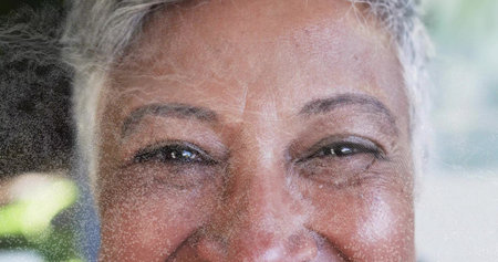 Gazing mature woman face showing fine lines and gray hair in garden, with frosted film overlay. Closeup, portrait, wrinkles, texture, speckled, translucent, bokehの写真素材